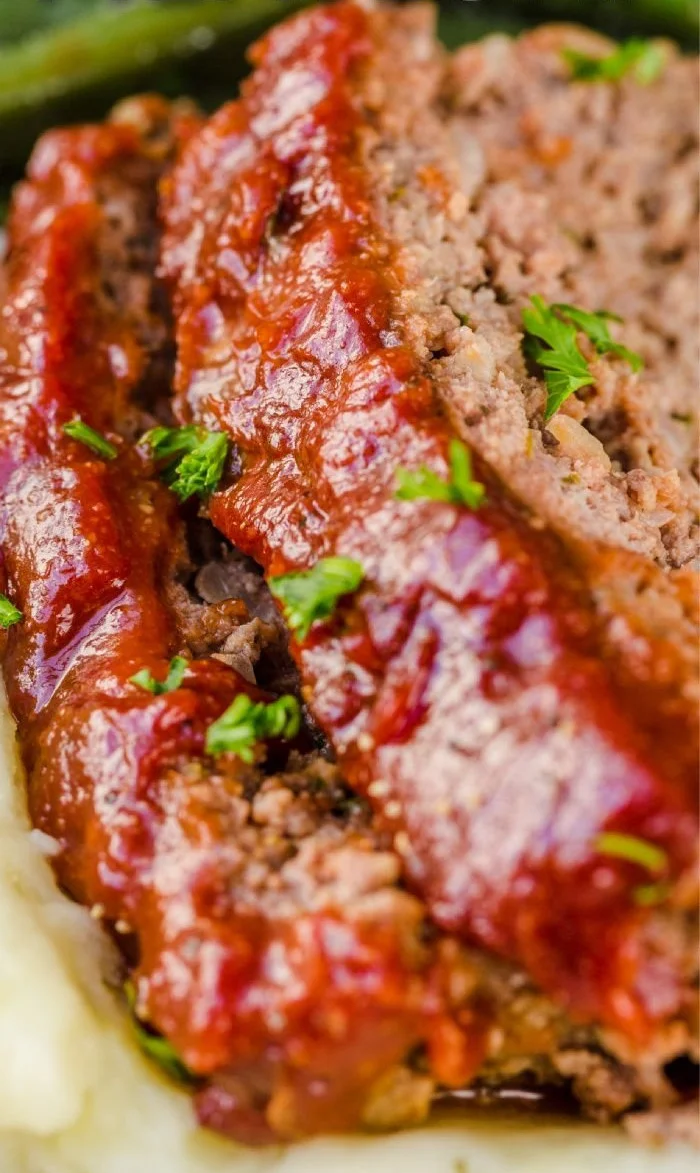 Sliced easy and excellent meatloaf on a plate, garnished with herbs.