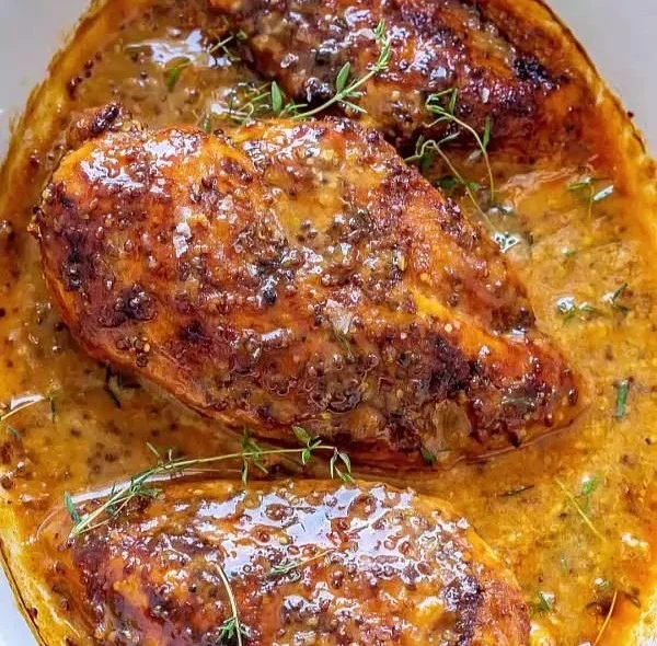 Delicious honey mustard chicken served on a plate with herbs and garnishes.