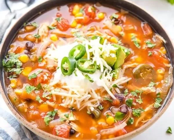 Bowl of Mexican tortilla soup topped with avocado and crispy tortilla strips.