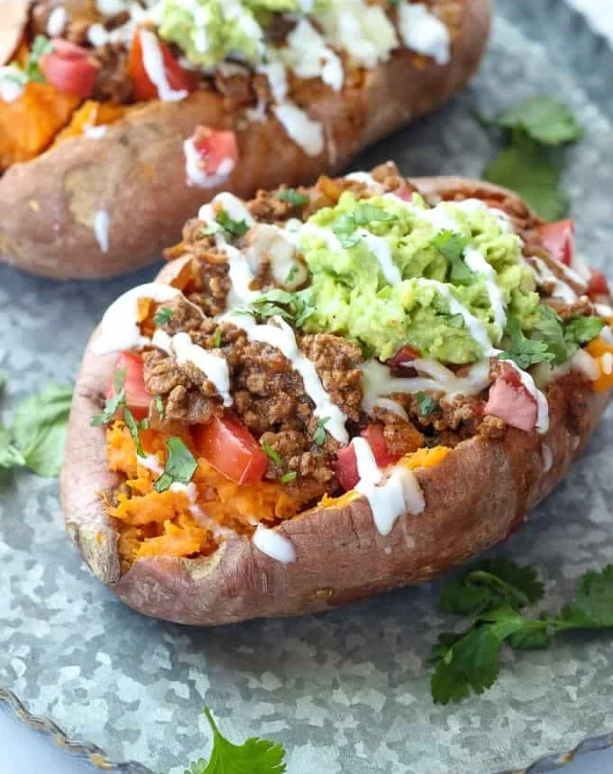 Taco stuffed sweet potatoes served with toppings and garnishes.